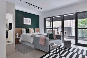 A modern bedroom with a bed, a grey sofa, a small table, and a balcony with a view. - Charlie Edição Jardim Paulista (São Paulo)
