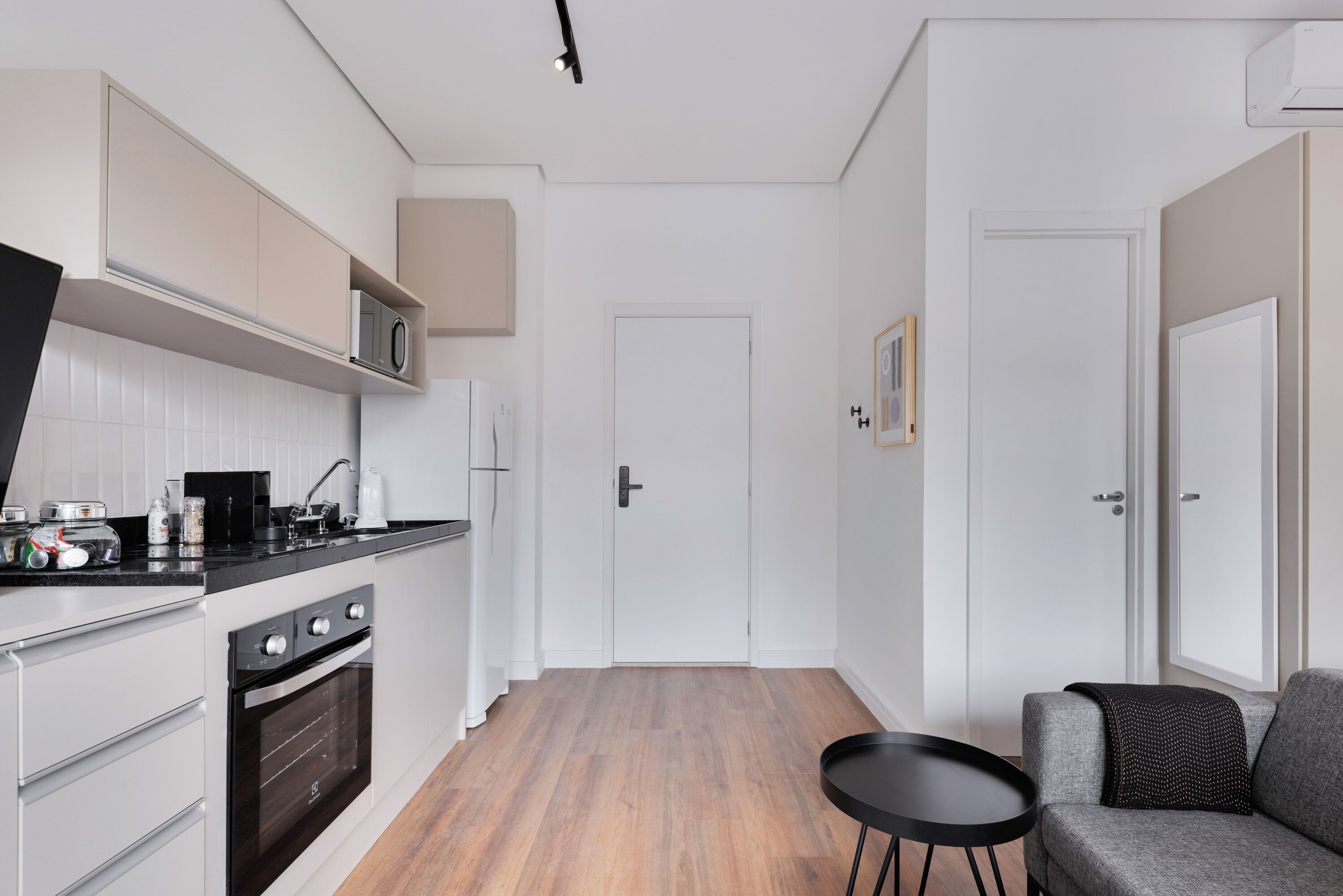 Une cuisine compacte avec des meubles blancs, un plan de travail noir et un four encastré.