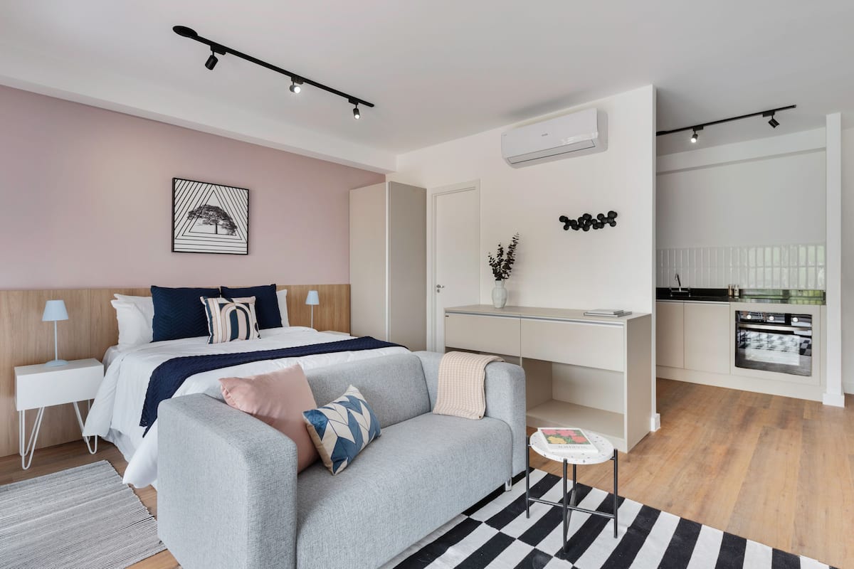 Un dormitorio moderno con una cama, mesitas de noche, un sofá, una pequeña mesa y una zona de cocina.