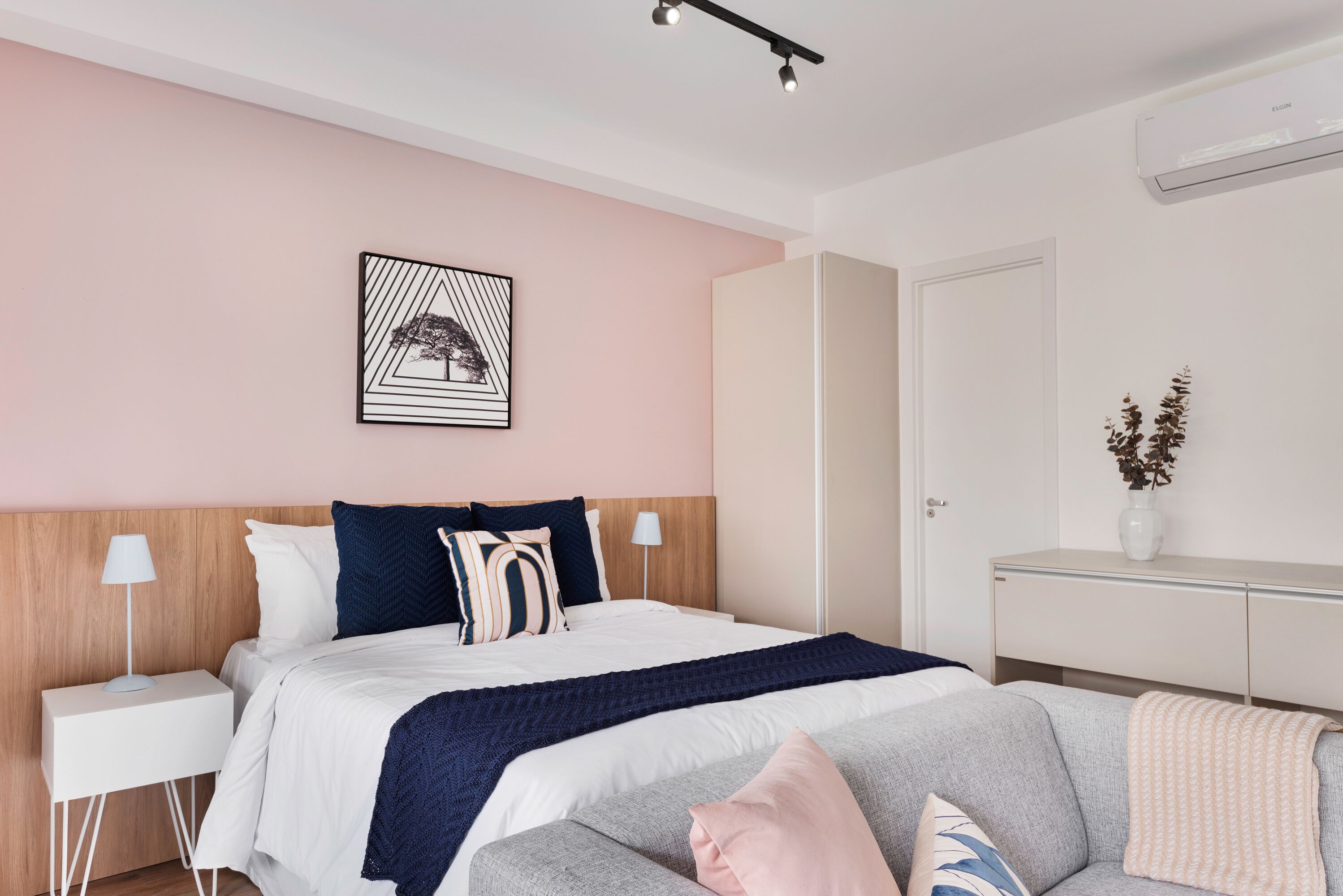 A modern bedroom with a bed, bedside tables, a sofa, a wall-mounted artwork, and a wardrobe.