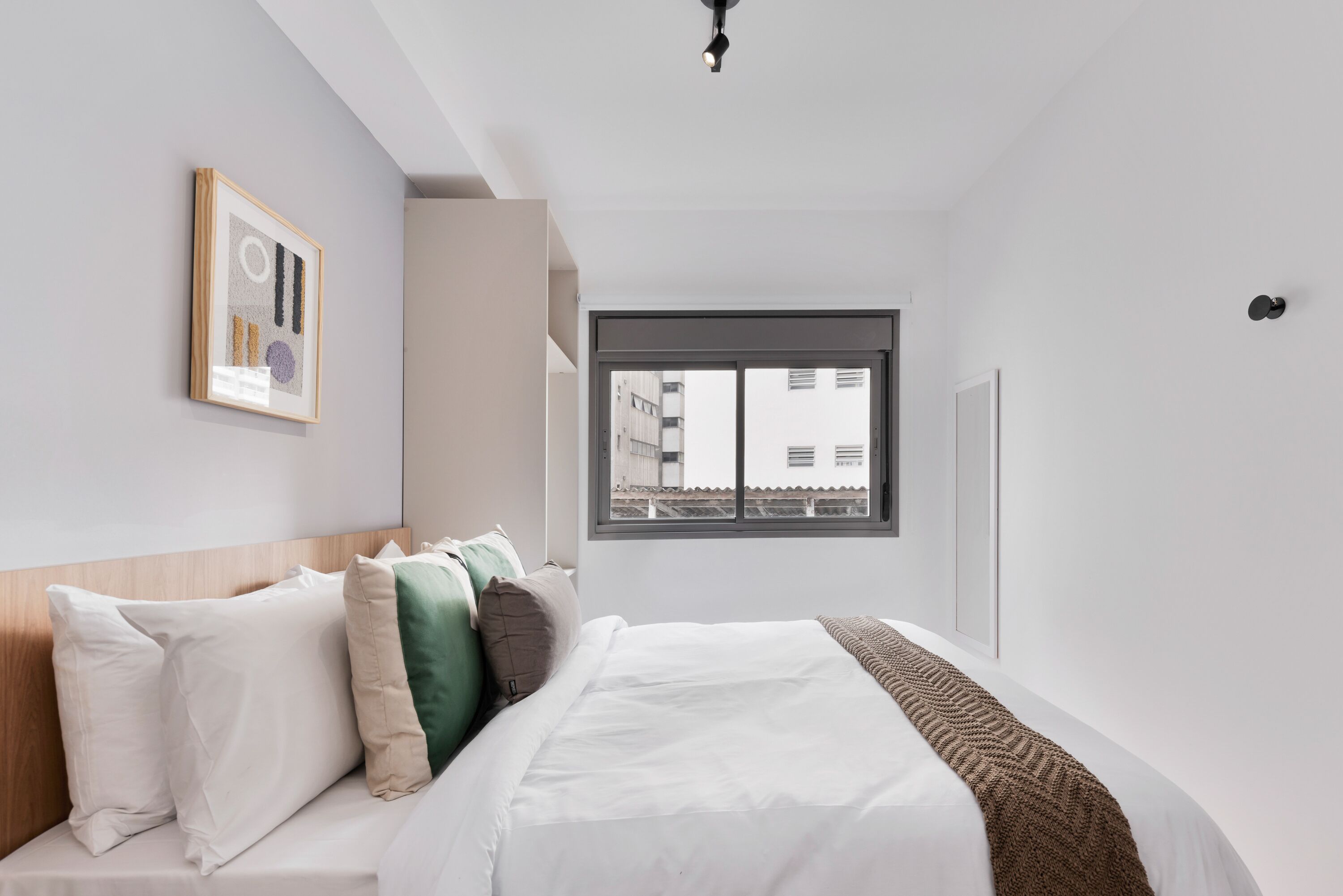 Un dormitorio moderno con una cama grande, una ventana con vistas a edificios y una obra de arte enmarcada en la pared.