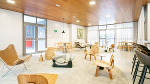 A spacious, modern interior with wooden flooring, a glass coffee table, and a variety of seating options including chairs and a sofa. - Charlie Edição Jardim Paulista (São Paulo)