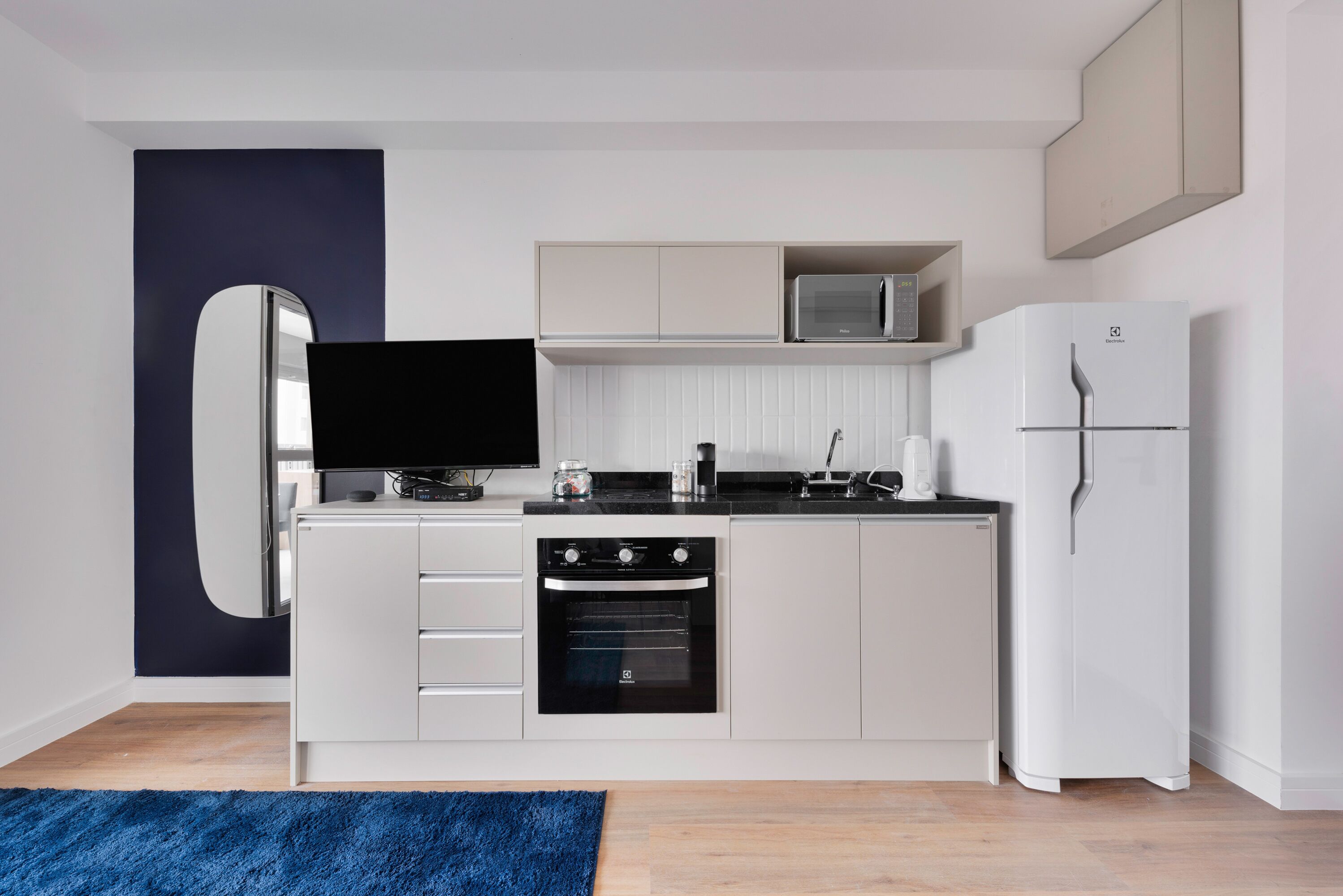 A modern kitchen with white cabinetry, a built-in oven, a microwave, and a refrigerator.