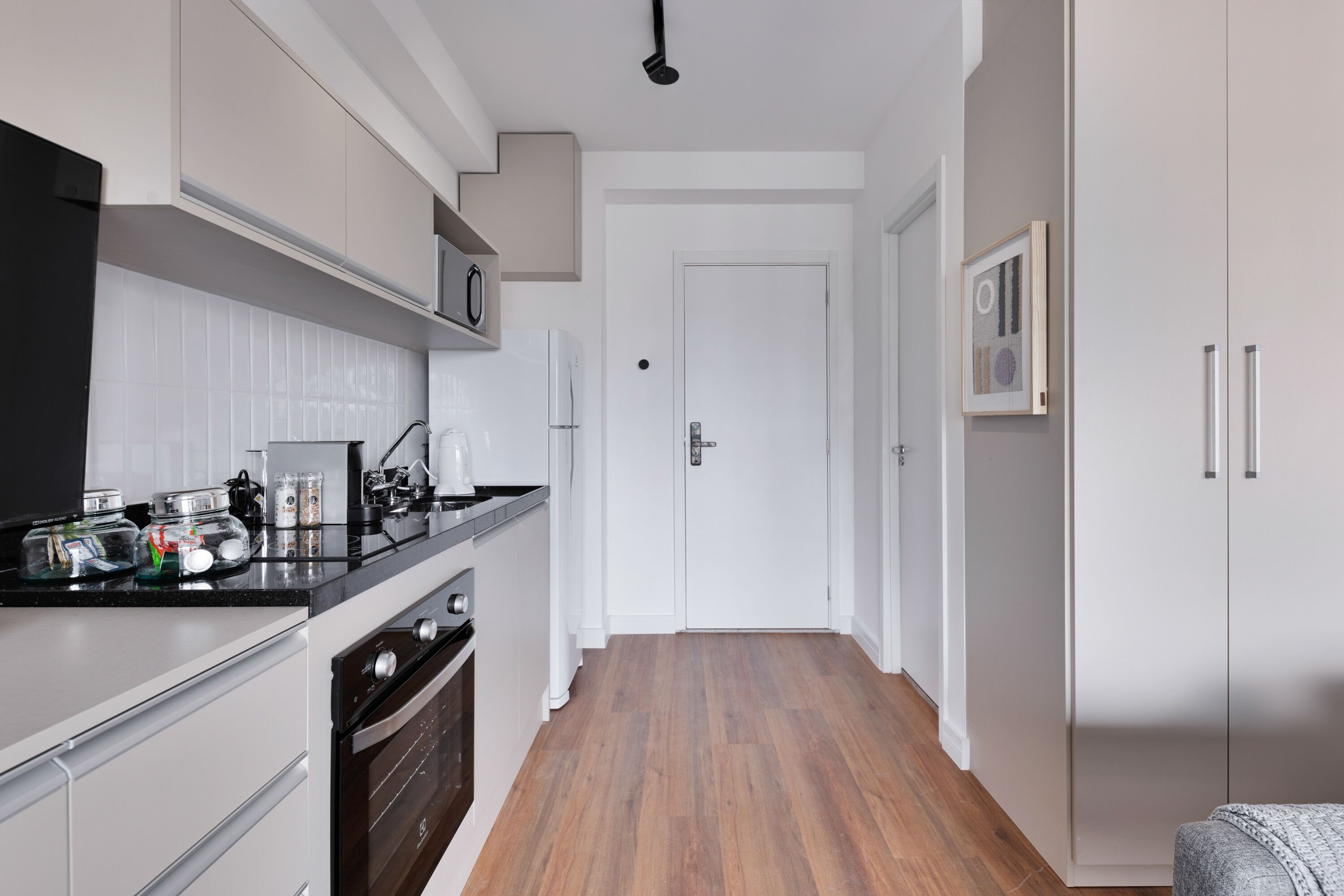 A modern kitchen with white cabinetry, a black countertop, and a wooden floor.