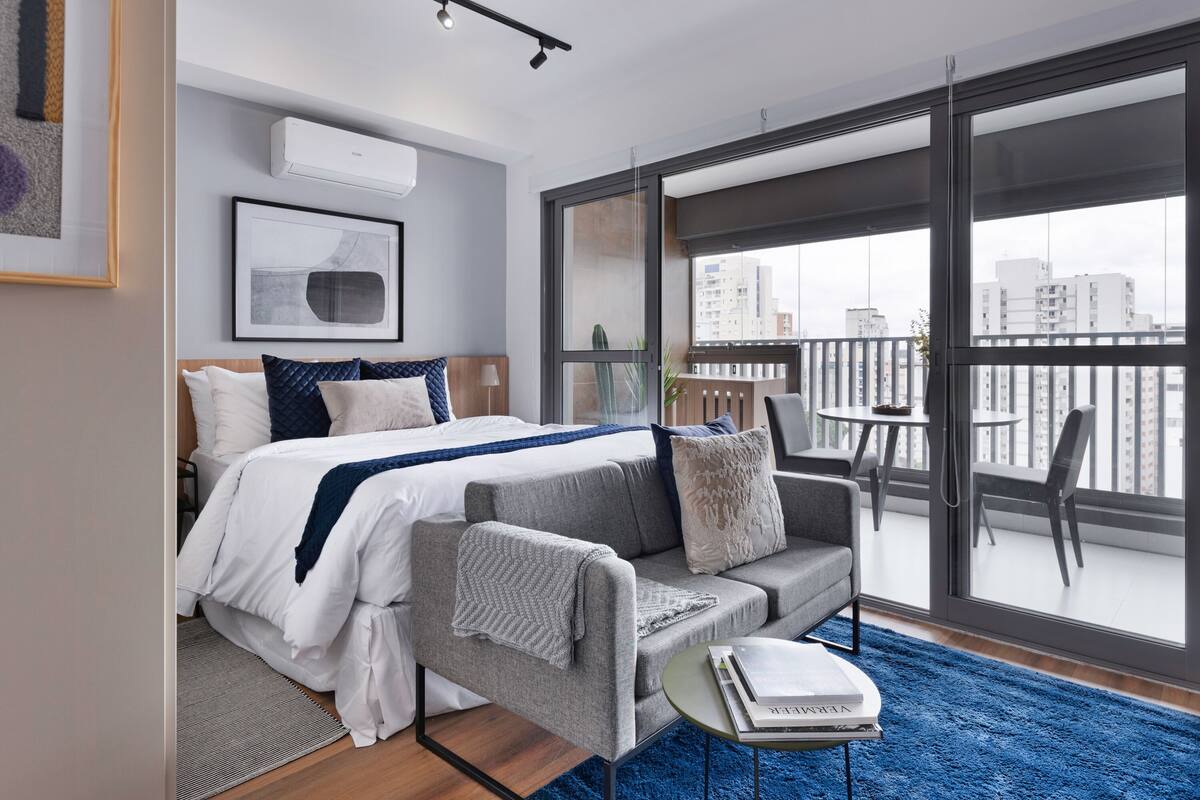 Un dormitorio moderno con cama, sofá y balcón con vista a la ciudad.