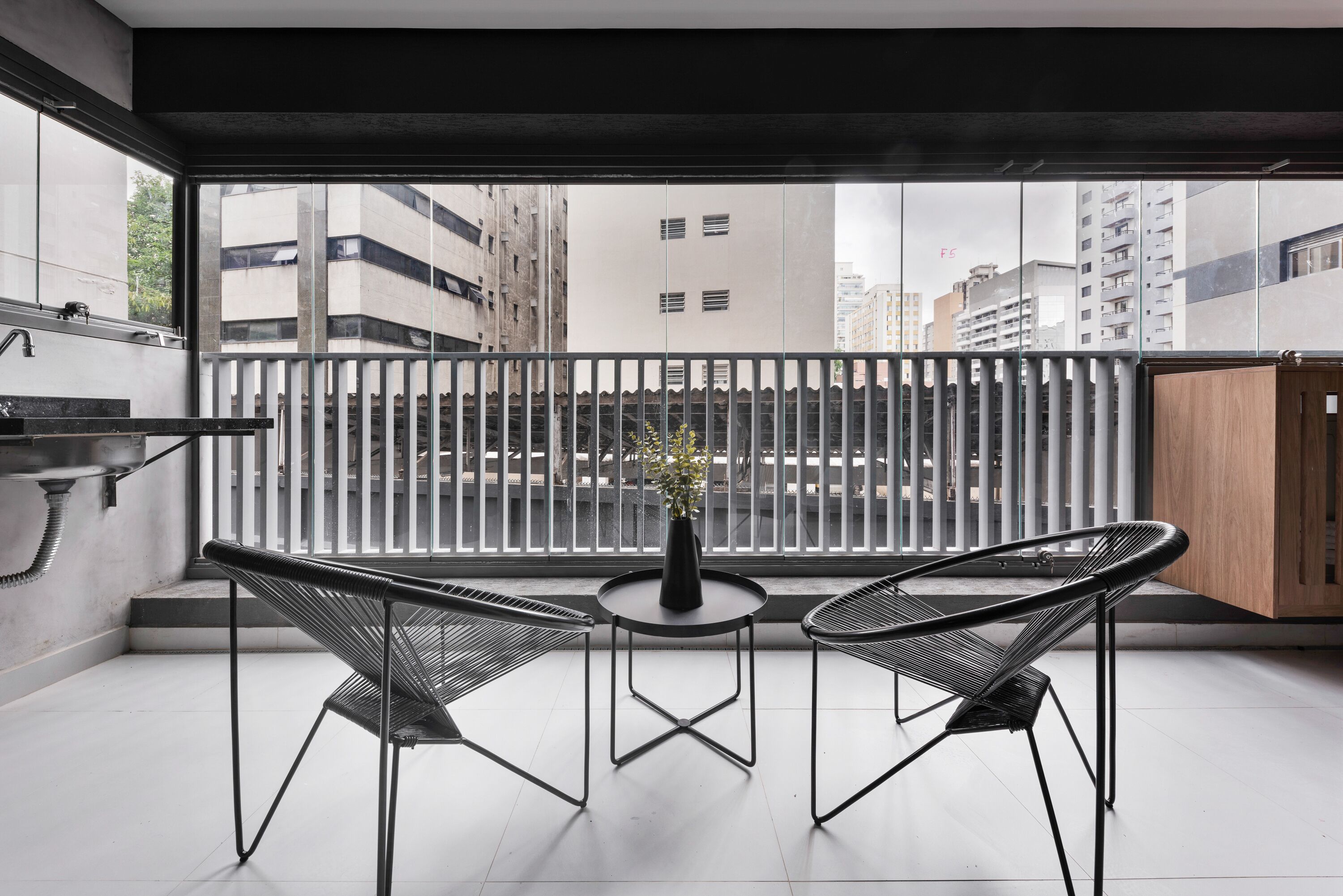 A balcony with two chairs, a small table, and a vase with flowers.