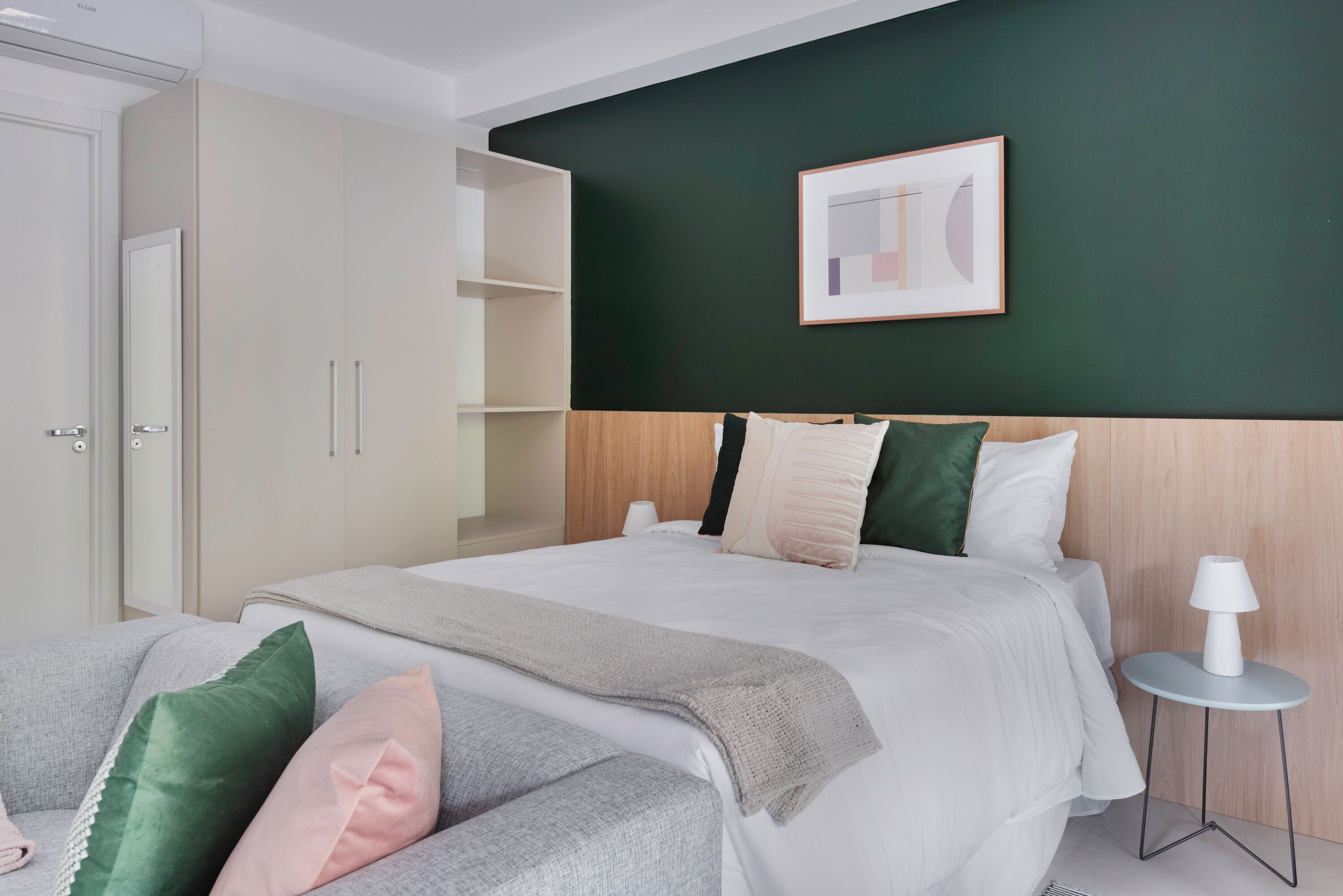 A modern bedroom with a bed, a side table, a wardrobe, and a framed picture on the wall.