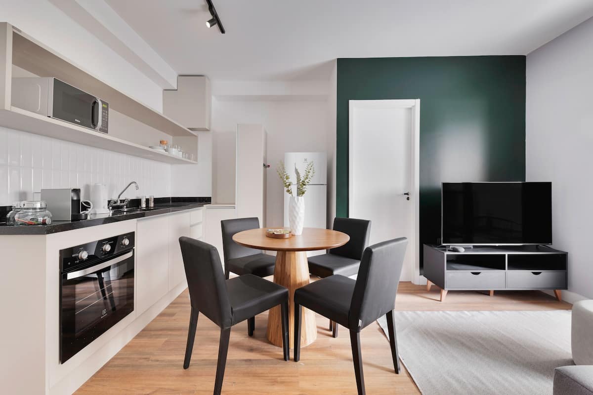 Una cocina moderna con horno empotrado y microondas, un comedor con mesa de madera y sillas negras, un televisor de pantalla plana y una pared de acento verde.