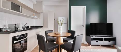 A modern kitchen with a built-in oven and microwave, a dining area with a wooden table and black chairs, a flat-screen TV, and a green accent wall.