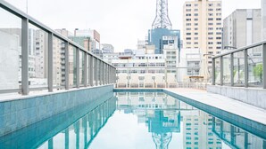 A modern indoor swimming pool with clear reflections of surrounding buildings, including a tall communication tower. - Charlie Edição Jardim Paulista (São Paulo)