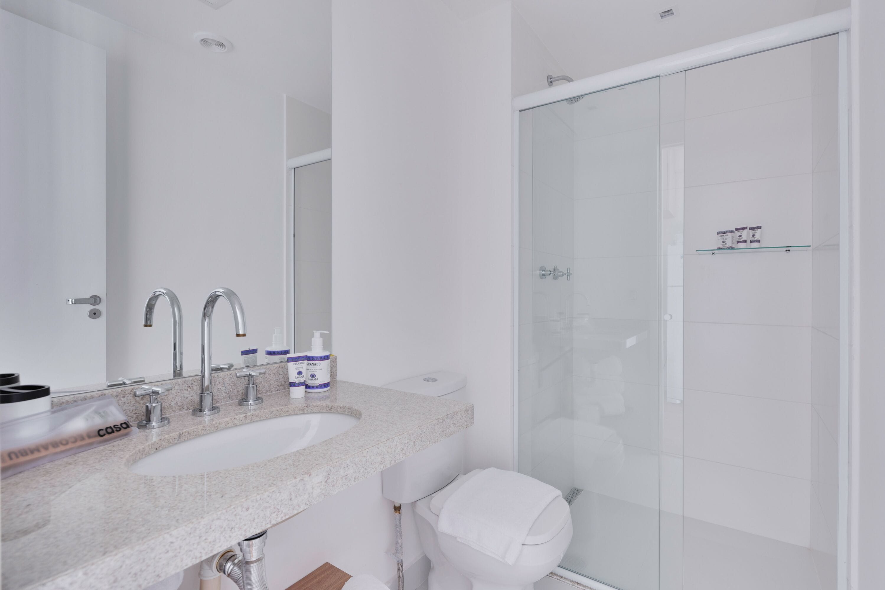 Een moderne badkamer met een wastafel, twee kraanwerk, toilet en een douche met glazen wanden.