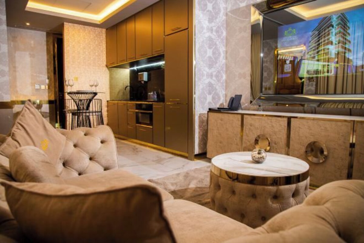 A modern living room with a sofa, a round coffee table, and a kitchen area with wooden cabinets and a built-in oven.
