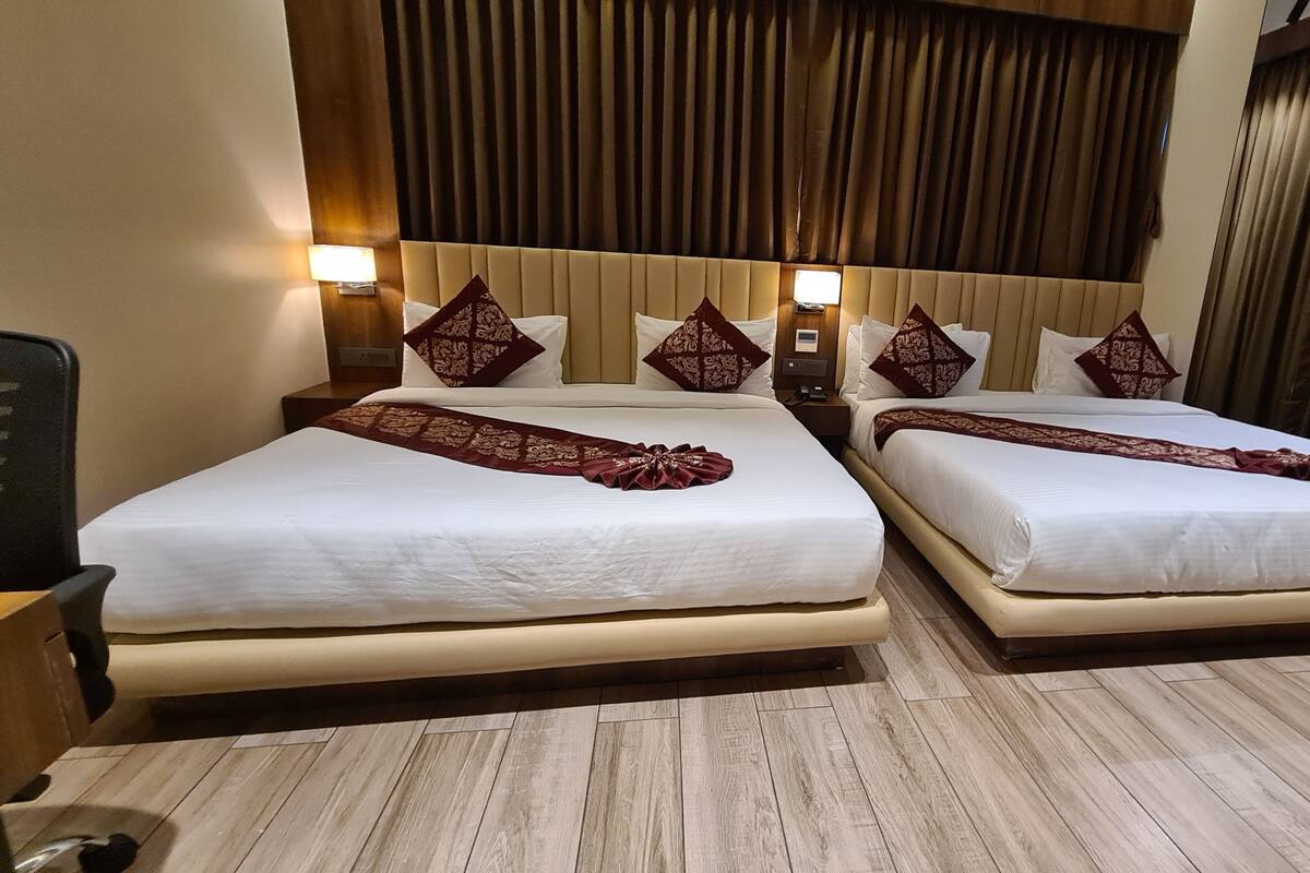 A hotel room with two beds, each with a white bedspread and a decorative red runner. The room has wooden flooring and a wooden headboard with vertical slats.