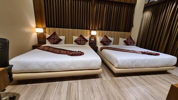 A hotel room with two beds, each with a white bedspread and a decorative red runner. The room has wooden flooring and a wooden headboard with vertical slats.
