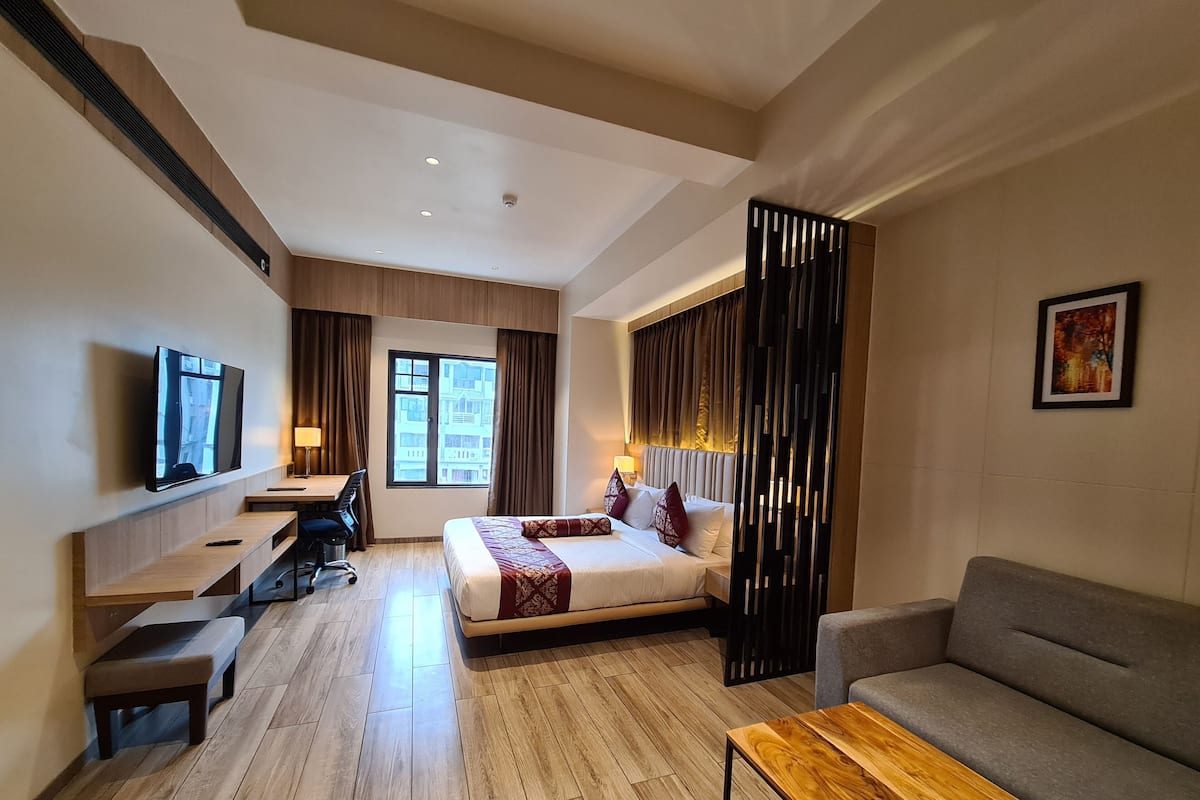 A hotel room with a bed, a sofa, a TV, a desk, and a window.