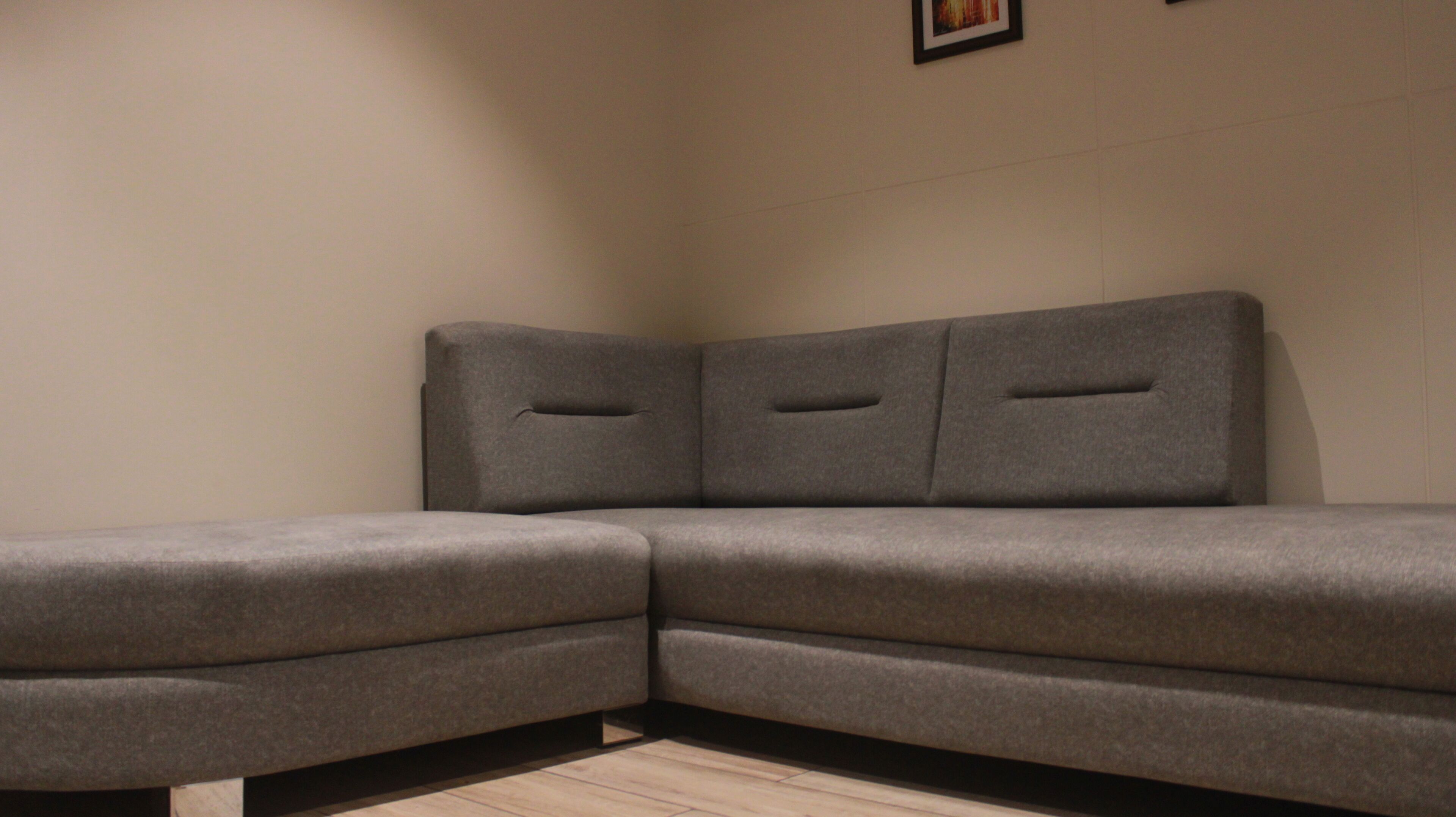 A corner sofa with a light-colored wall and a framed picture above it.