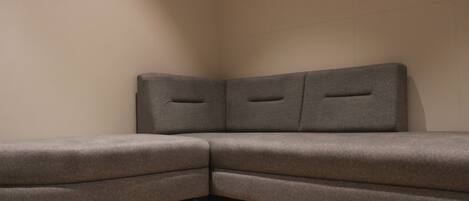 A corner sofa with a light-colored wall and a framed picture above it.