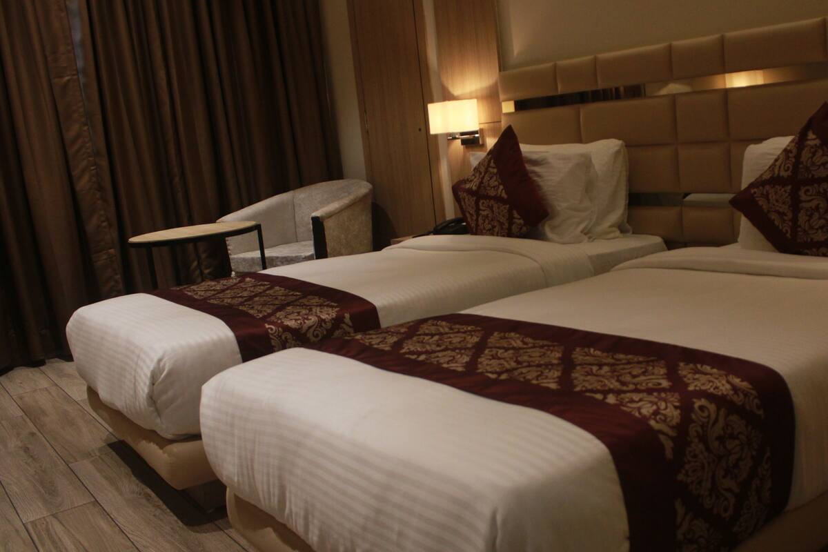 A hotel room with two beds, a chair, a table, and a lamp.