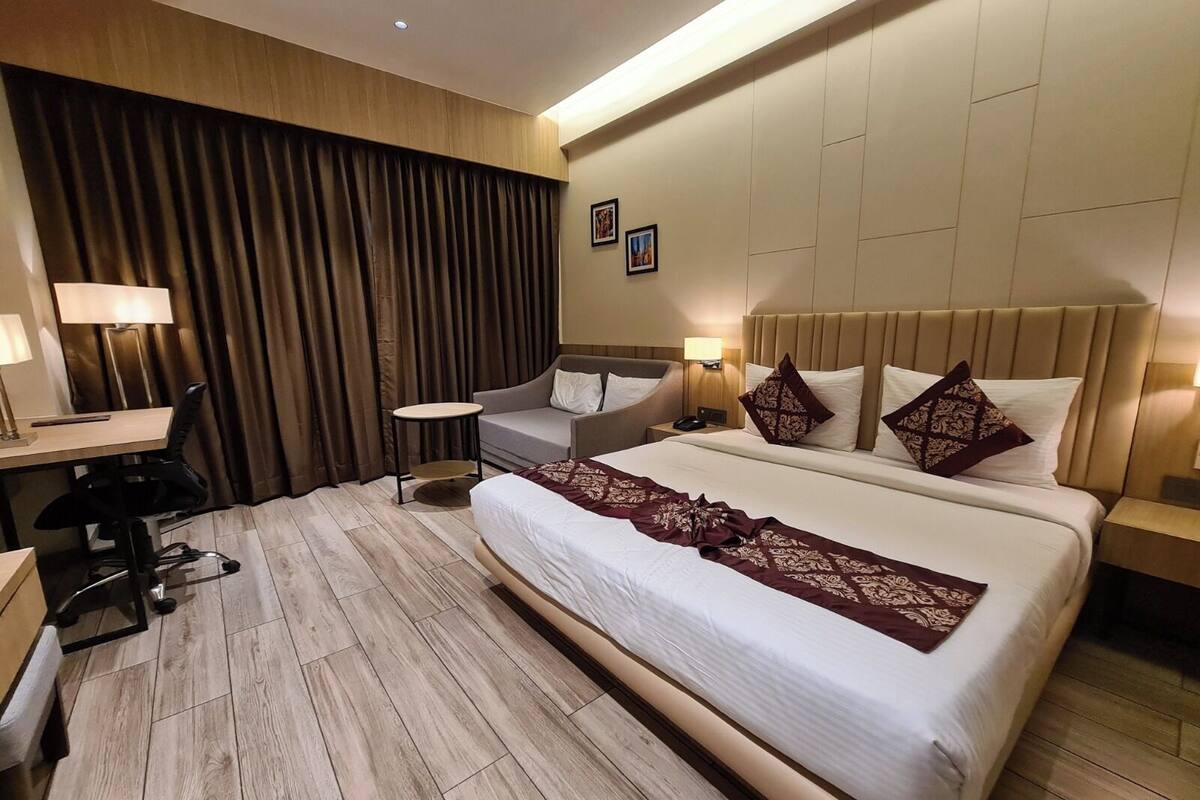 A hotel room with a large bed, a desk, a chair, a small table, and a sofa.
