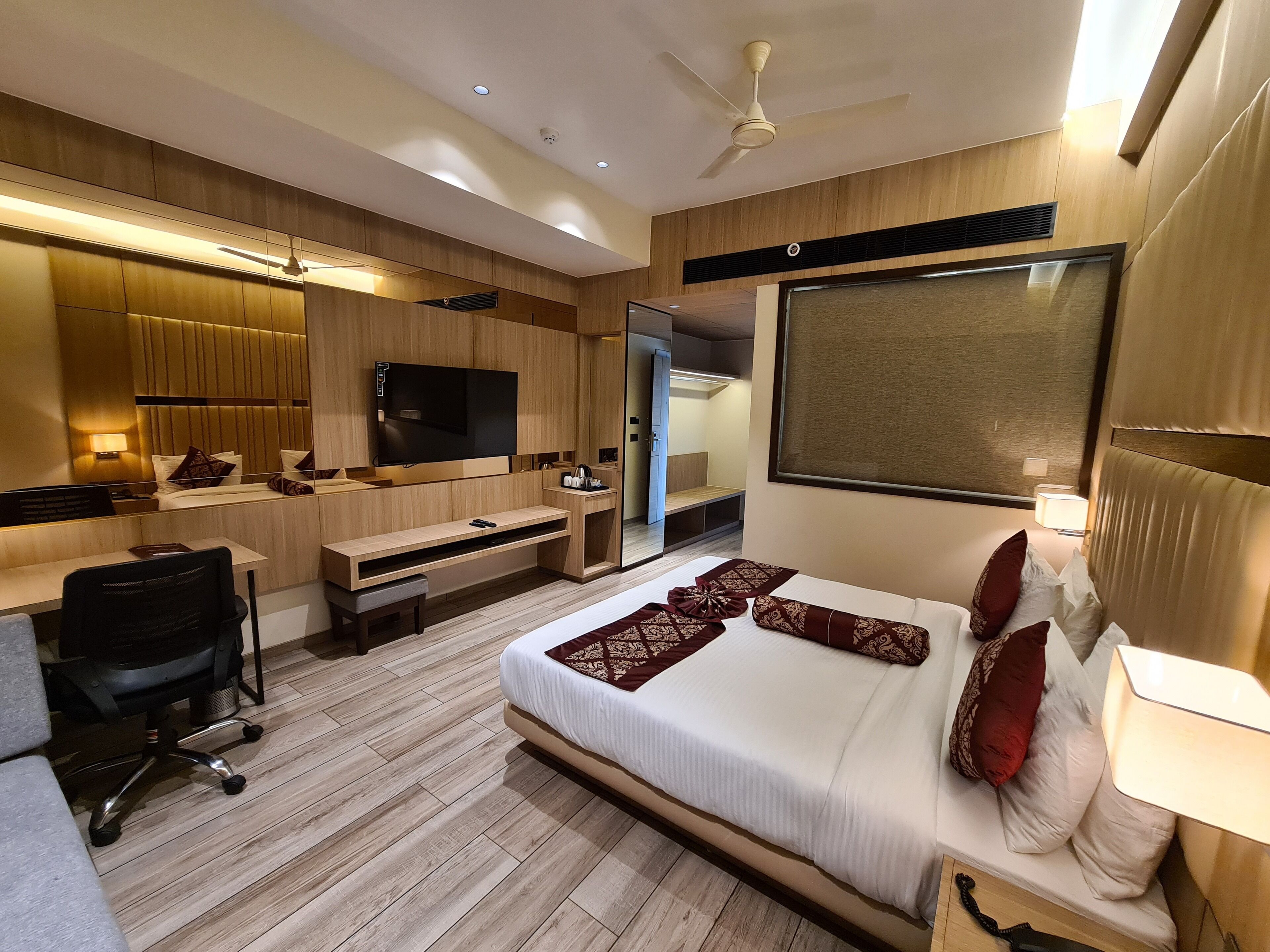 A modern hotel room with a large bed, a desk, a chair, a TV, and a ceiling fan.