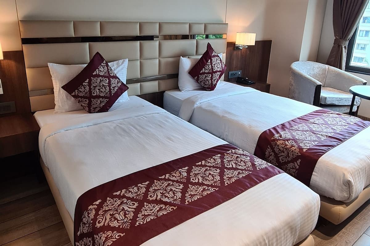 A hotel room with two beds, a headboard, artwork on the wall, and a wooden floor.