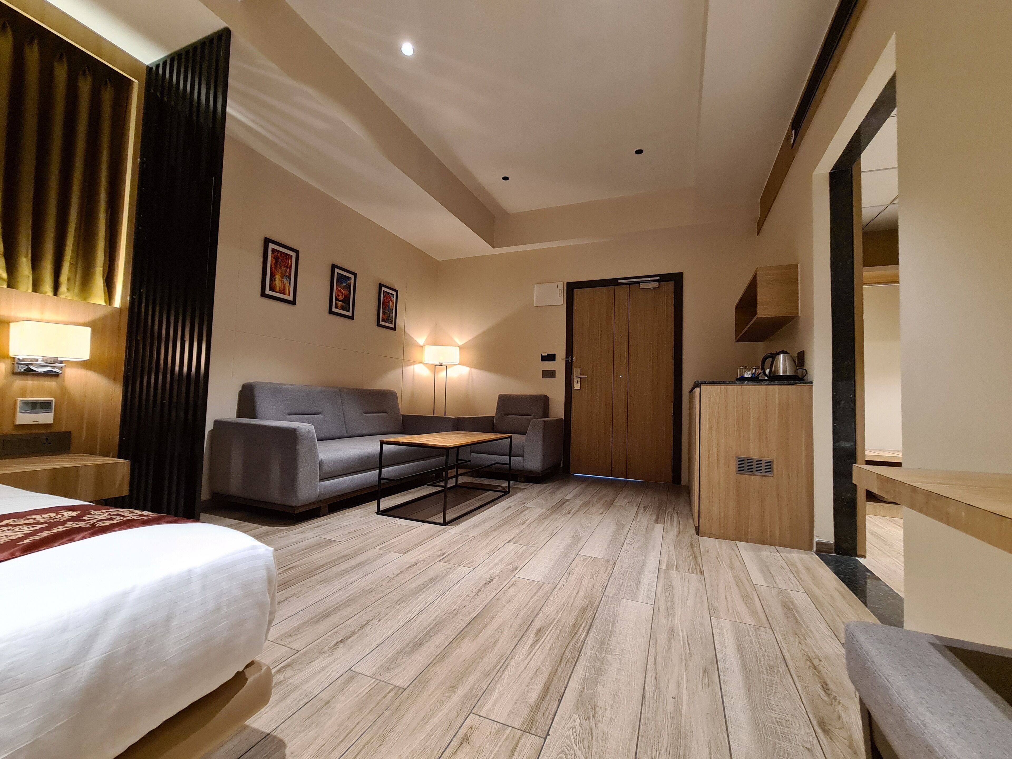 A hotel room with a bed, a sofa, a small table, a desk, a wardrobe, and a lamp.