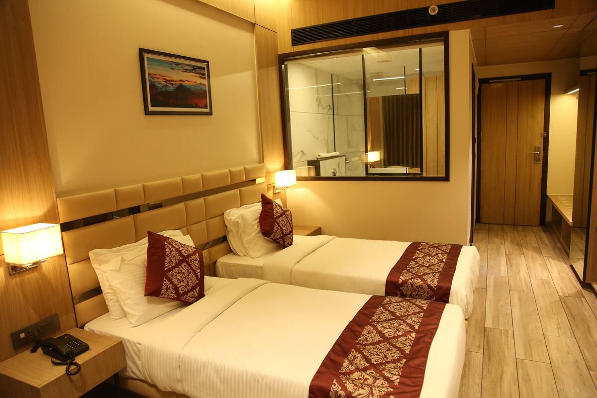 A hotel room with two beds, a nightstand with a phone, a painting on the wall, and a large mirror.
