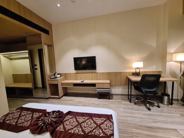 Una habitación de hotel con cama, escritorio, silla, televisor y lámpara.