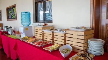 Montaje de buffet con diferentes alimentos, un dispensador de agua y platos apilados.