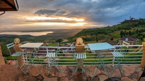 A terrace with a view of a lake and hills, featuring outdoor furniture and a stone floor.