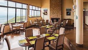A restaurant with multiple tables and chairs, large windows with a view, and a brick wall.