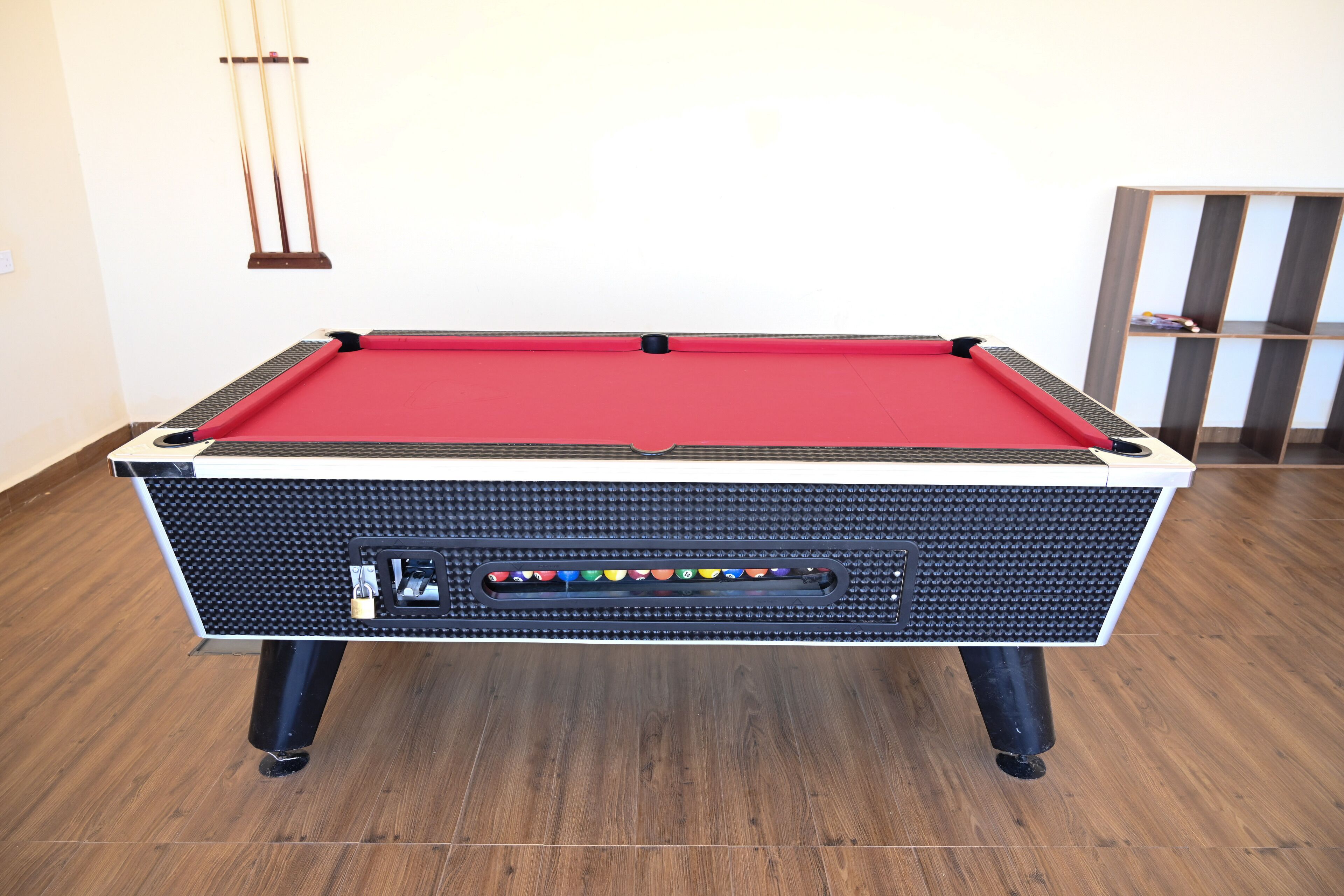 A pool table with a red felt top, black textured sides, and a built-in electronic scoreboard.