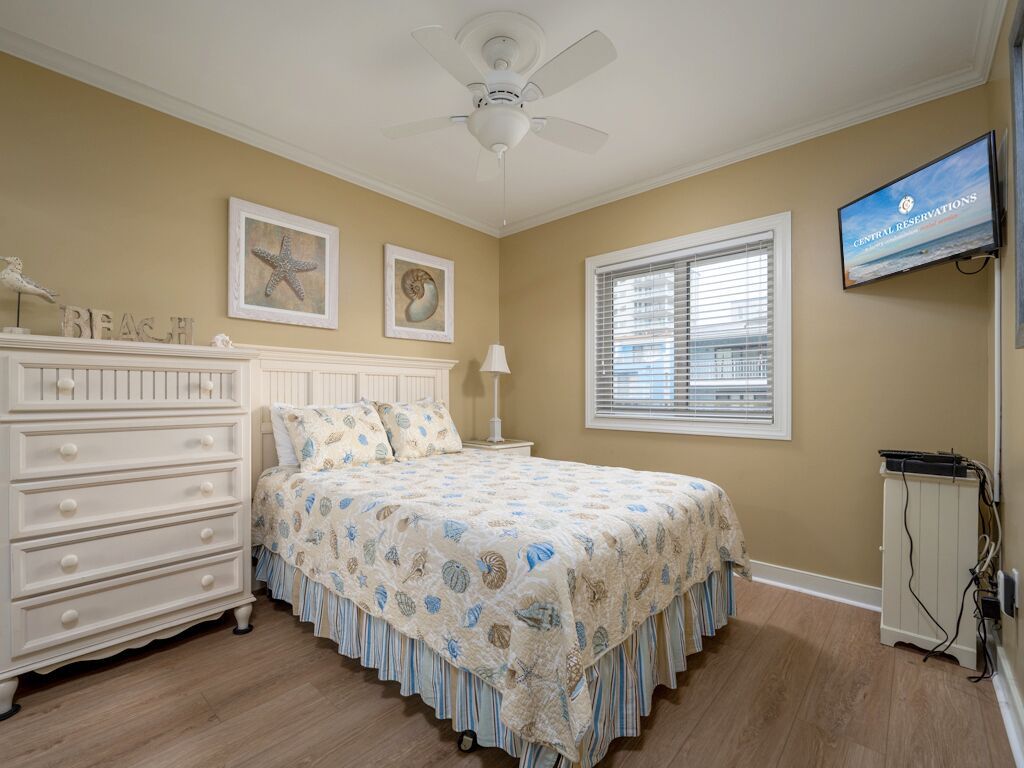 A bedroom with a bed, dresser, ceiling fan, artwork, window, and TV.