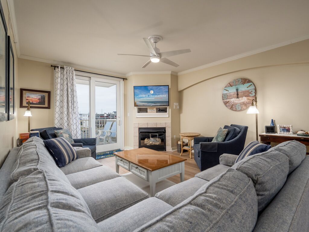 A living room with a sofa set, a coffee table, a fireplace, a television, and a balcony with a view.