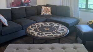 Una sala de estar con un sofá modular, una mesa de centro redonda, una araña y un cuadro grande de una vaca.