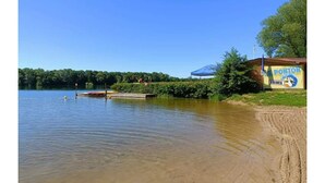 A lakeside view with a dock, a small building with a blue canopy, and a sign reading "E PONTON LAIVES". - The fountains (Laives)