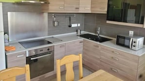 A compact kitchen with a built-in oven, a microwave, a sink, and wooden cabinets. - The fountains (Laives)