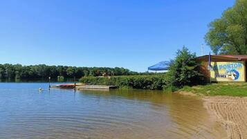 Vista sul lago con un pontile, un piccolo edificio con una tenda blu e un cartello con su scritto “E PONTON LAIVES”.