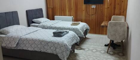 A bedroom with two beds, a TV mounted on the wall, a chair, and a patterned rug.