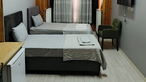 Ein Schlafzimmer mit einem großen Bett, einem kleinen Tisch, einem Sessel, einem Fernseher und einem Fenster mit Vorhängen.