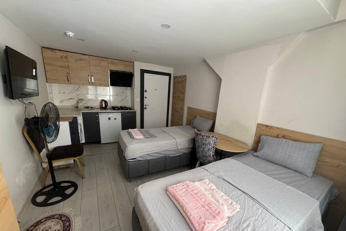 Ein kleines Hotelzimmer mit Küchenzeile, zwei Betten, einem Tisch und einem Ventilator.