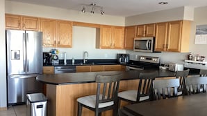 A modern kitchen with wooden cabinets, stainless steel appliances, a central island with bar stools, and a small trash bin. - Spacious 4BD 3Bth townhouse on the peninsula! (Onamia)
