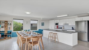 A modern kitchen with white cabinets, a stainless steel refrigerator, and a dining area with wooden chairs and a table set for six.