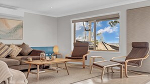 Ein modernes Wohnzimmer mit großem Fenster, einer Couch, zwei Sesseln, einem Couchtisch und einem kleinen Beistelltisch.