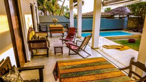A covered outdoor seating area with a pool, wooden furniture, and a colorful woven table runner. - Beach villa KANDU near Hikkaduwa (Kumarakanda Dodanduwa)