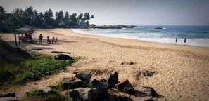A beach with a thatched structure and people near the water.