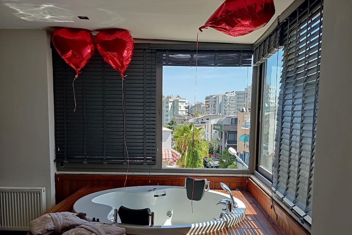 A modern bathroom with a freestanding bathtub, wooden benches, and a view of the city through large windows.