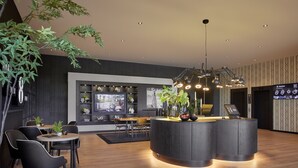 Un moderno vestíbulo de hotel con un mostrador de recepción central, área de descanso y una pantalla grande que muestra información meteorológica.