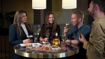 A group of people seated around a round table with food and drinks, in a room with a modern design and pendant lighting.