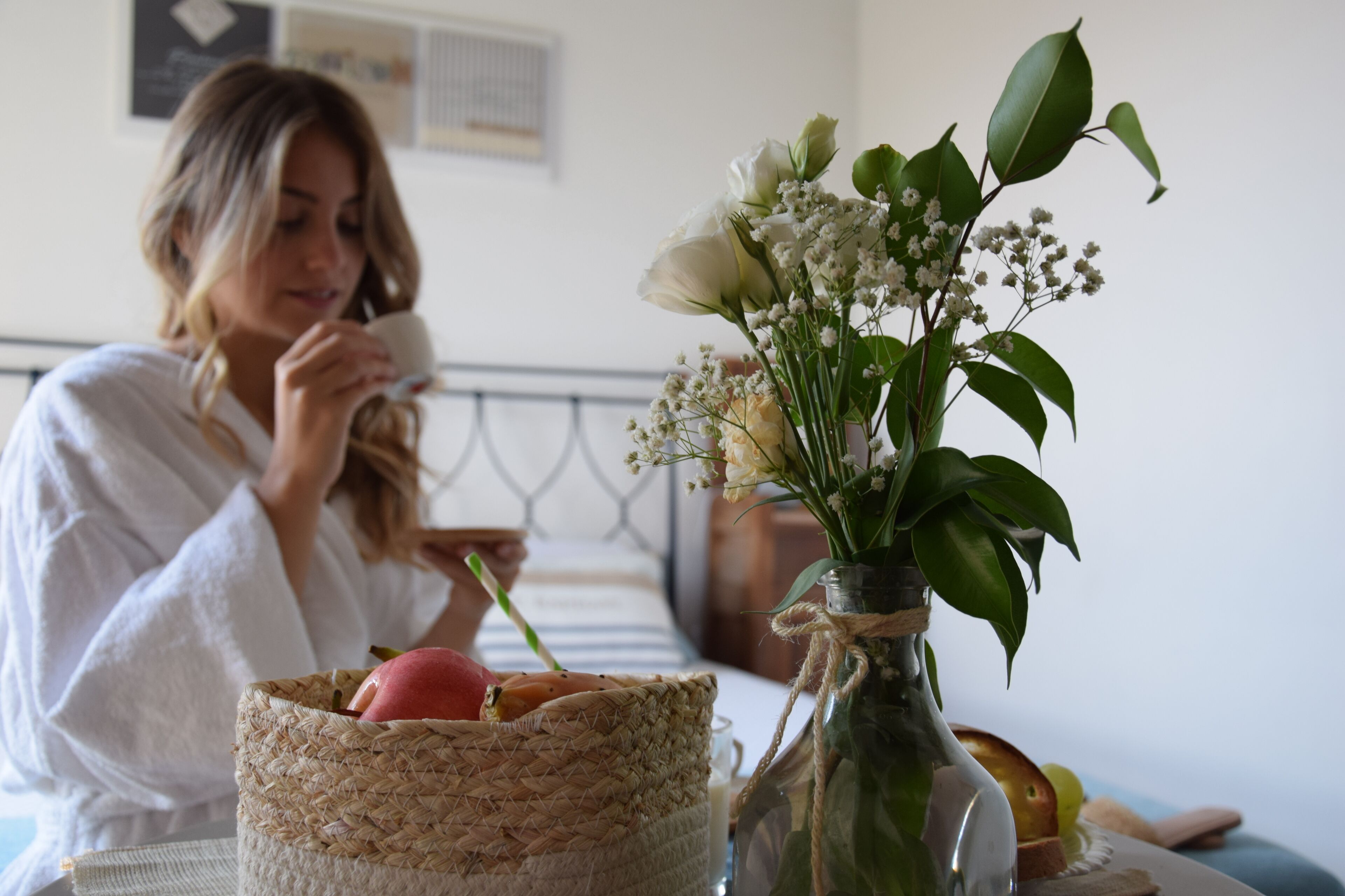 Eine Person sitzt an einem Tisch mit einem gewebten Korb, der Brot und ein Glas mit Blumen enthält.